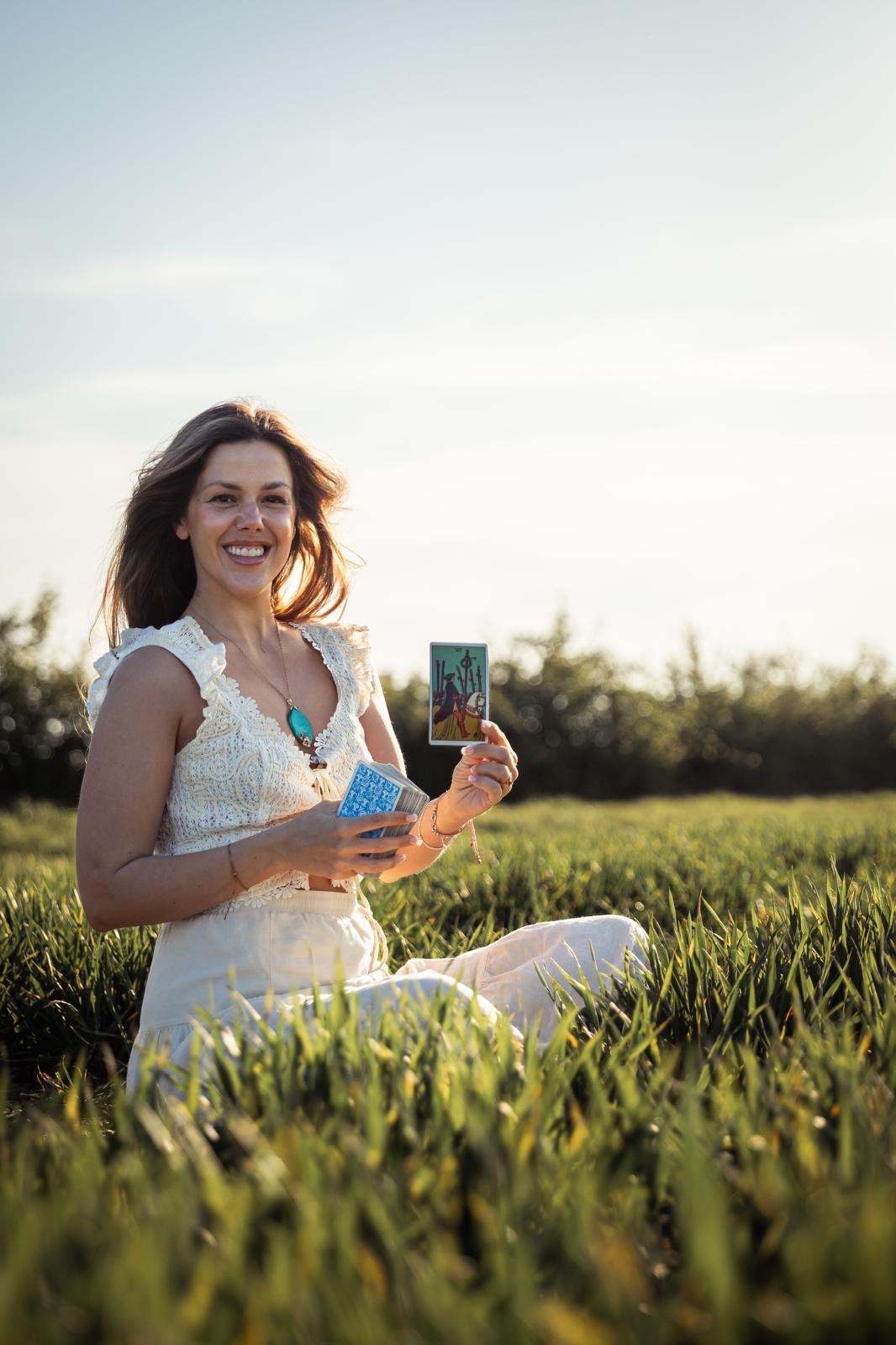Eva Nunn standing in a sun-drenched field holding a tarot card
